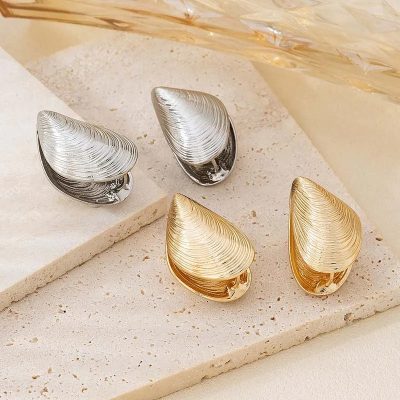 Silver and gold shell-shaped earrings displayed on a beige textured surface, ideal for stylish accessory shopping at Monalisa Store.