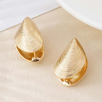 Shimmering gold shell-shaped earrings on a beige background, perfect for elegant accessories and jewelry shoppers.
