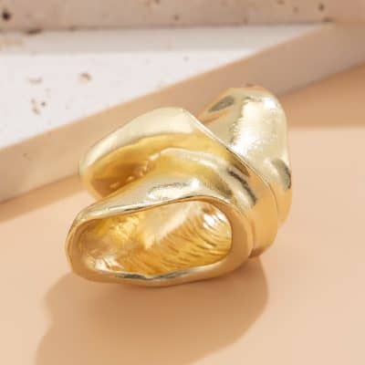 Golden metallic fashion ring with abstract, flowing design on a neutral background. Perfect for luxury jewelry and high-end accessories.