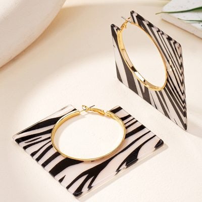 Golden hoop earrings with black and white striped geometric design, displayed on matching black and white patterned stands, ideal for stylish accessories at Monalisa Store.
