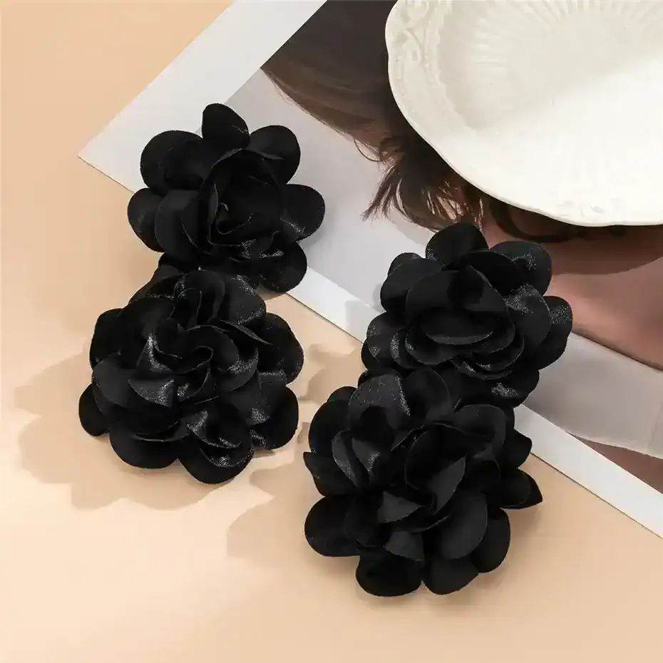 Black fabric flower earrings displayed on a desk with a white hat and photo in the background.