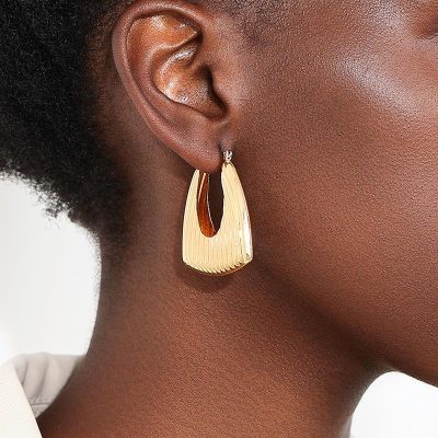 Shiny gold statement earring on a woman's ear, close-up, stylish jewelry accessory, perfect for fashion and beauty enhancements.