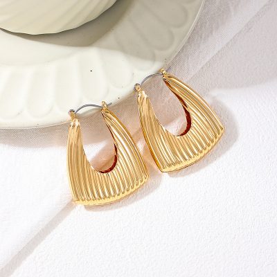 Shiny gold textured hoop earrings displayed on a white ceramic dish for stylish accessory showcasing.