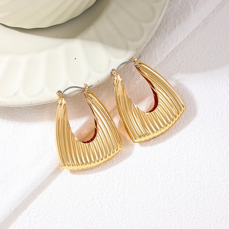 Shiny gold textured hoop earrings displayed on a white ceramic dish for stylish accessory showcasing.
