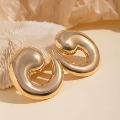 Elegant gold and silver swirl earrings on soft beige fabric, showcasing stylish and luxury jewelry from Monalisa Store. Perfect for enhancing your fashionable look with high-quality accessories.