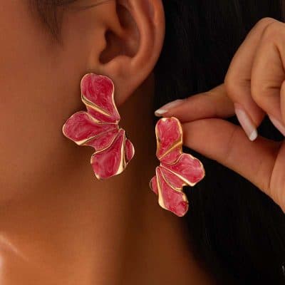 Bright pink floral statement earrings with gold accents, worn by a woman showcasing elegant jewelry style. Perfect for fashionable accessories and trendy earring designs.