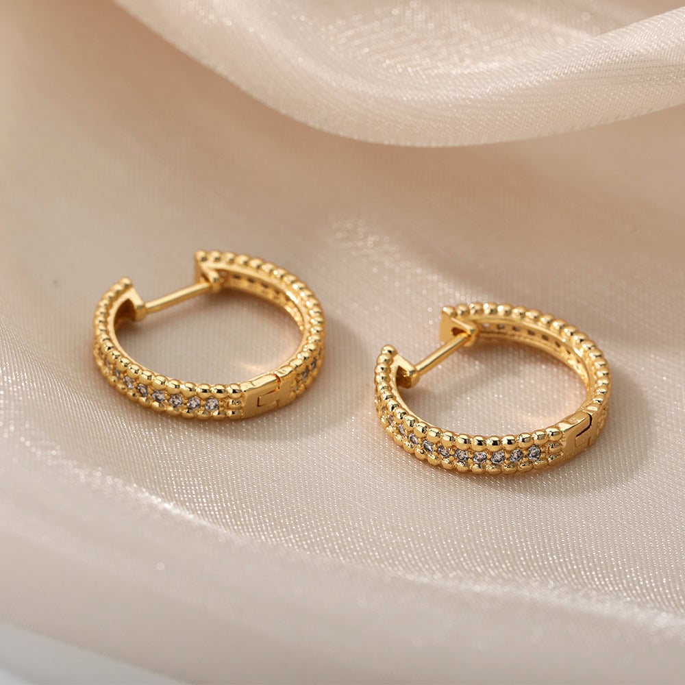Shiny gold hoop earrings with embedded crystals displayed on silky fabric.