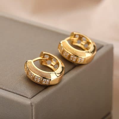 Shiny gold earrings with embedded sparkling stones on a beige jewelry box.