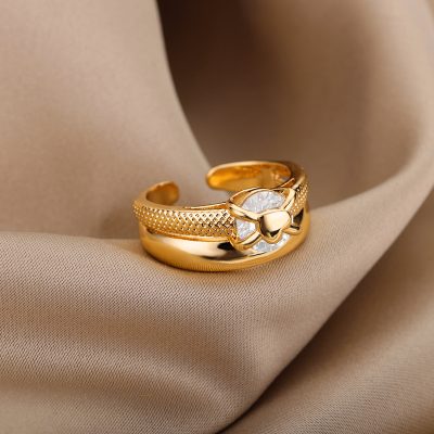 Intricate gold ring with a heart-shaped gemstone and bow design, showcased on smooth beige fabric, enhancing its luxurious appeal.