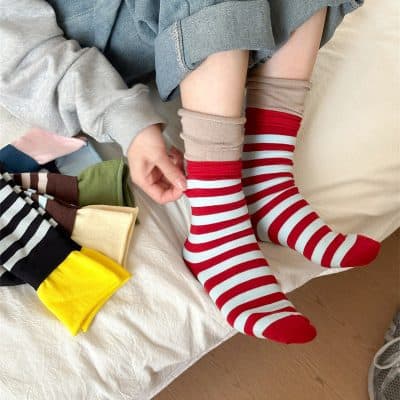 Bright red and white striped socks displayed on a person's legs, with a variety of colorful socks folded nearby, showcasing Monalisa Medical's diverse sock collection for comfortable and stylish foot wear.