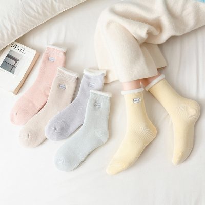 Pastel-colored cozy socks displayed on a white bed with a book, perfect for comfortable, stylish footwear, emphasizing quality and softness for warmer and colder seasons.