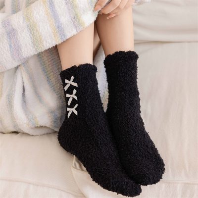 Cozy black fleece slippers with white bow details, perfect for relaxing at home or as a gift, featuring soft, warm material ideal for cold weather.