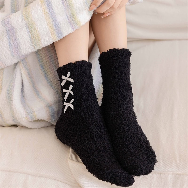 Cozy black fleece slippers with white bow details, perfect for relaxing at home or as a gift, featuring soft, warm material ideal for cold weather.