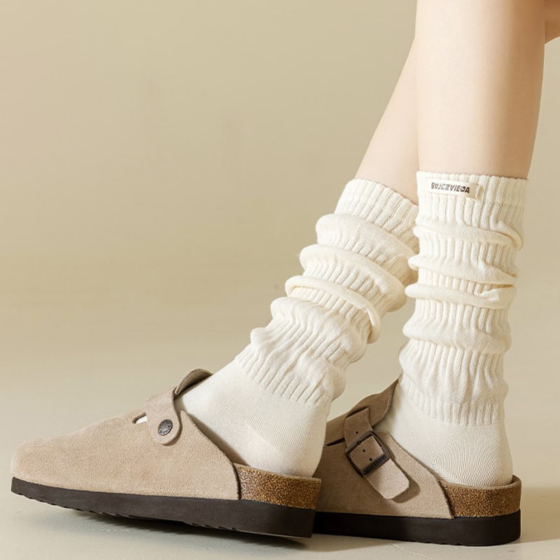 White cozy socks with logo on cuff, comfortable beige slippers with adjustable buckle and textured sole, ideal for indoor wear, featured on a model's feet for a stylish and cozy look at Monalisa Medical Store.