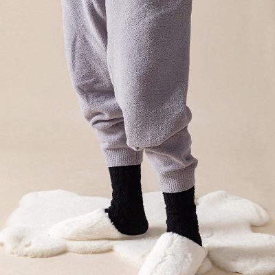 Soft cozy grey sweatpants with black socks and plush slippers, laid on a fluffy white rug, promoting comfortable and stylish loungewear from Monalisa Medical's opt store.