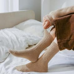 Soft beige knee-high socks on person sitting on bed, cozy indoor setting, comfortable casual fashion, warm knitted socks, Monalisa Medical store focus, opt for comfort and style.