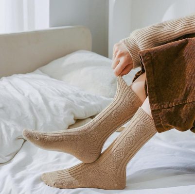 Soft beige knee-high socks on person sitting on bed, cozy indoor setting, comfortable casual fashion, warm knitted socks, Monalisa Medical store focus, opt for comfort and style.
