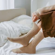 Comfy beige socks on person putting them on in a cozy bedroom, promoting comfortable foot wear and home relaxation lifestyle.