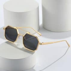 Gold frame sunglasses with dark lenses on white geometric blocks for Monalisa Store optometry and eyewear fashion.