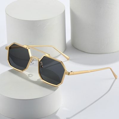 Gold frame sunglasses with dark lenses on white geometric blocks for Monalisa Store optometry and eyewear fashion.