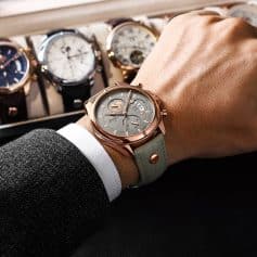 Shiny rose gold wristwatch with chronograph features, beige leather strap, and multiple watch displays, showcased on a person's wrist amid a collection of luxury watches at Monalisa Store.