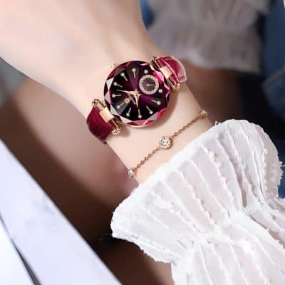 Luxurious women's wristwatch featuring a deep red, faceted gemstone-inspired dial with diamond accents, paired with elegant jewelry; perfect for stylish fashion and luxury accessories.