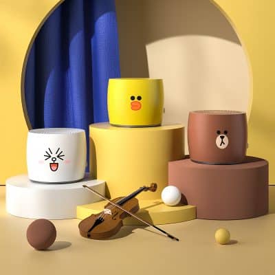 Cute cartoon face speaker with colorful design in playful studio setting with musical instrument and geometric shapes.