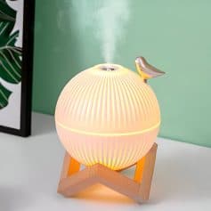 Vaporizer diffuser lamp with a spherical design, emitting mist for aromatherapy, placed on a wooden stand in a modern space.