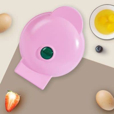 Pink silicone egg separator on beige and gray background with eggs, berries, and baking ingredients.