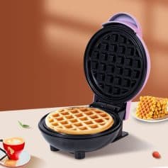 Delicious waffle in a cute pink electric waffle maker with breakfast toppings on a cozy kitchen countertop.