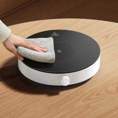 Ultrasonic jewelry cleaner on a wooden table, hand wiping the device with a microfiber cloth, perfect for jewelry and eyeglass cleaning, high-quality and easy to use for household opt needs.