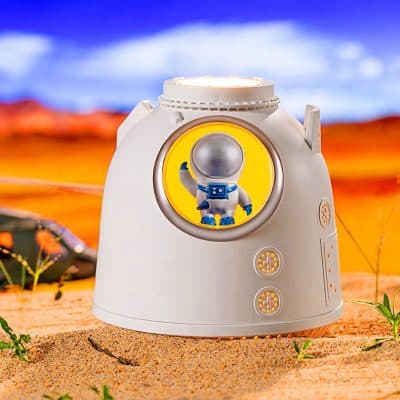 NASA astronaut figure on a white dome-shaped device with control buttons in a desert landscape with blue sky and clouds, likely a promotional or novelty item.