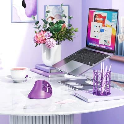 Bright workspace with a laptop, purple mouse, and decorative pink flowers in a white vase on a clean marble desk, perfect for digital or office work, featuring vibrant, modern decor.