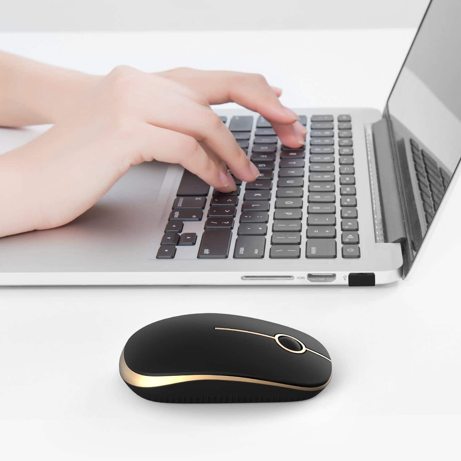 Hands typing on a silver laptop keyboard with a wireless black and gold mouse on a white desk, representing online shopping for medical supplies or eyewear accessories.