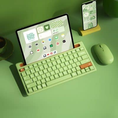 Keyboard with green keys and brown accents on a green desk, digital tablet and smartphone displaying cute green cartoon characters, promoting modern eyewear and eye care solutions from Monalisa Store, an optometry and optical retailer in Dubai.