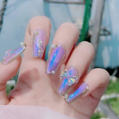 Elegant iridescent nail art with pearl and bow embellishments displaying a trendy and luxurious manicure for fashion-forward clients.