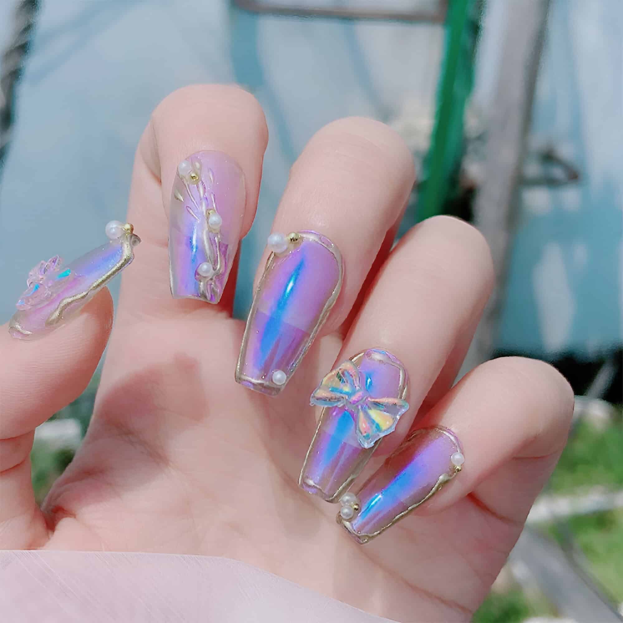 Elegant iridescent nail art with pearl and bow embellishments displaying a trendy and luxurious manicure for fashion-forward clients.