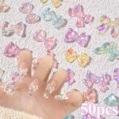 Colorful iridescent bow-shaped nail art accessories for manicure, with a hand displaying 3D bow nails, on a textured white surface, with