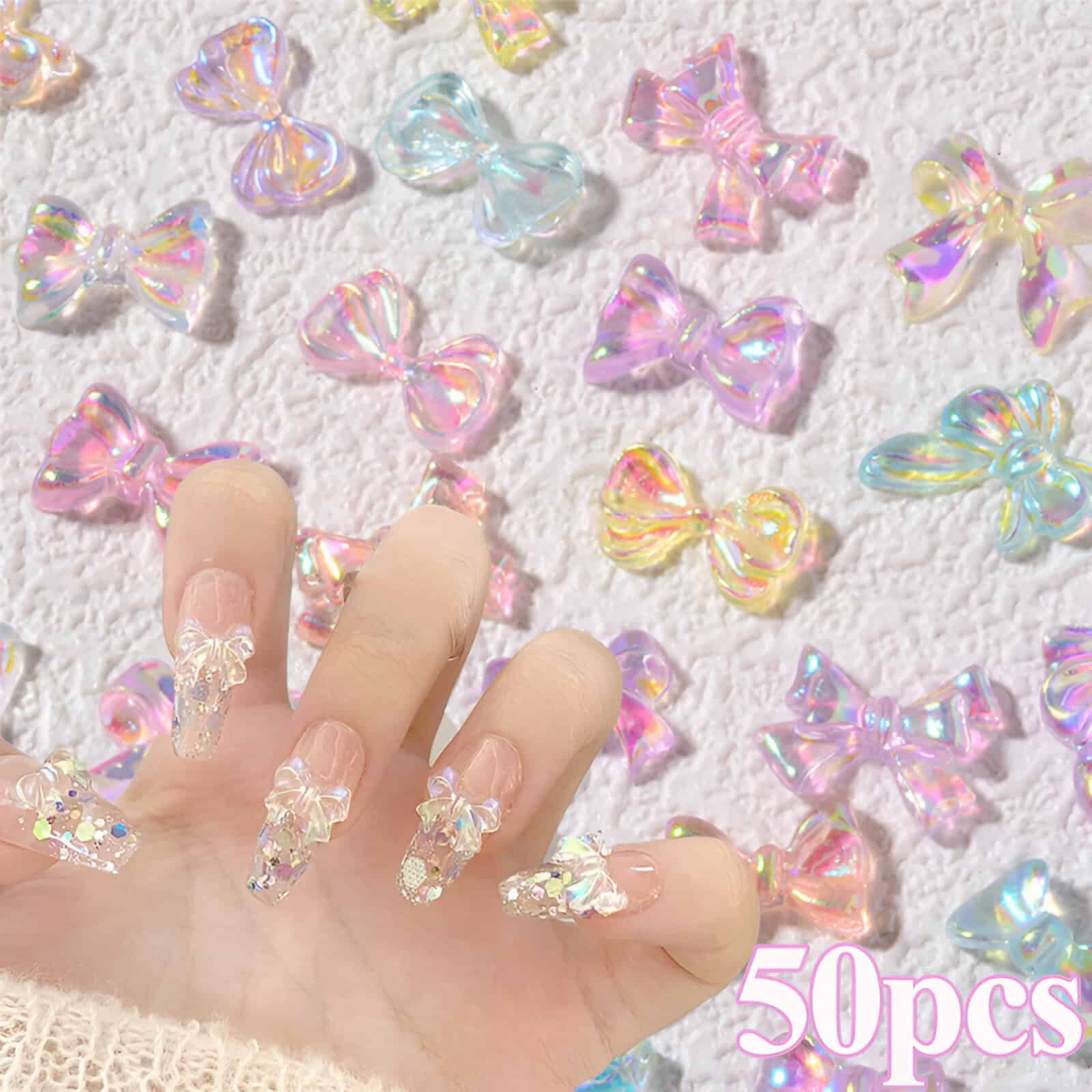 Colorful iridescent bow-shaped nail art accessories for manicure, with a hand displaying 3D bow nails, on a textured white surface, with "50pcs" text, perfect for nail design and decoration.