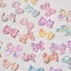 Colorful iridescent bow-shaped charms on textured white background, ideal for nail art, jewelry making, and craft supplies. Trending accessories for personalized, stylish DIY projects.