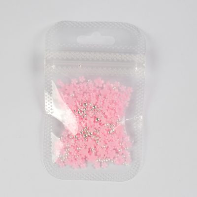 Colorful pink flower and silver nail art rhinestones in transparent packaging for nail decoration and beauty salons.
