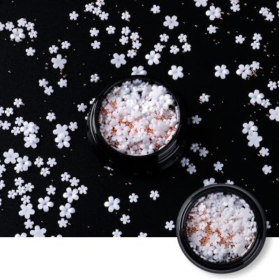 White floral-shaped nail glitter decorations in jars for manicure embellishments.