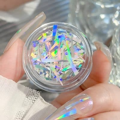 Holographic nail art glitter in a small clear container, perfect for enhancing nail designs with a shiny, iridescent finish.