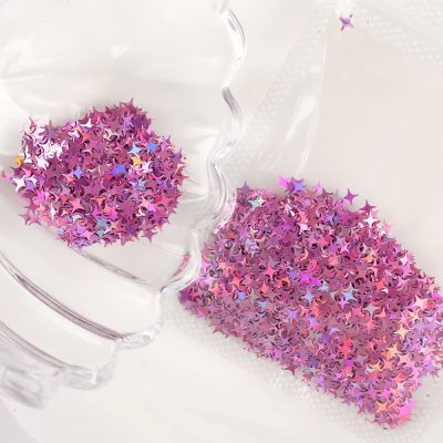 Shimmering pink star-shaped nail art confetti in a clear glass bowl with some scattered on the white surface, perfect for beauty and cosmetic nail decoration at Monalisa Store.