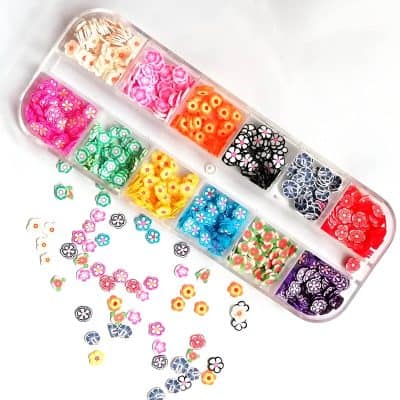 Colorful floral nail art decorations in a storage container, ideal for beauty salons and personal manicures. Bright, vibrant designs perfect for enhancing nail aesthetics.
