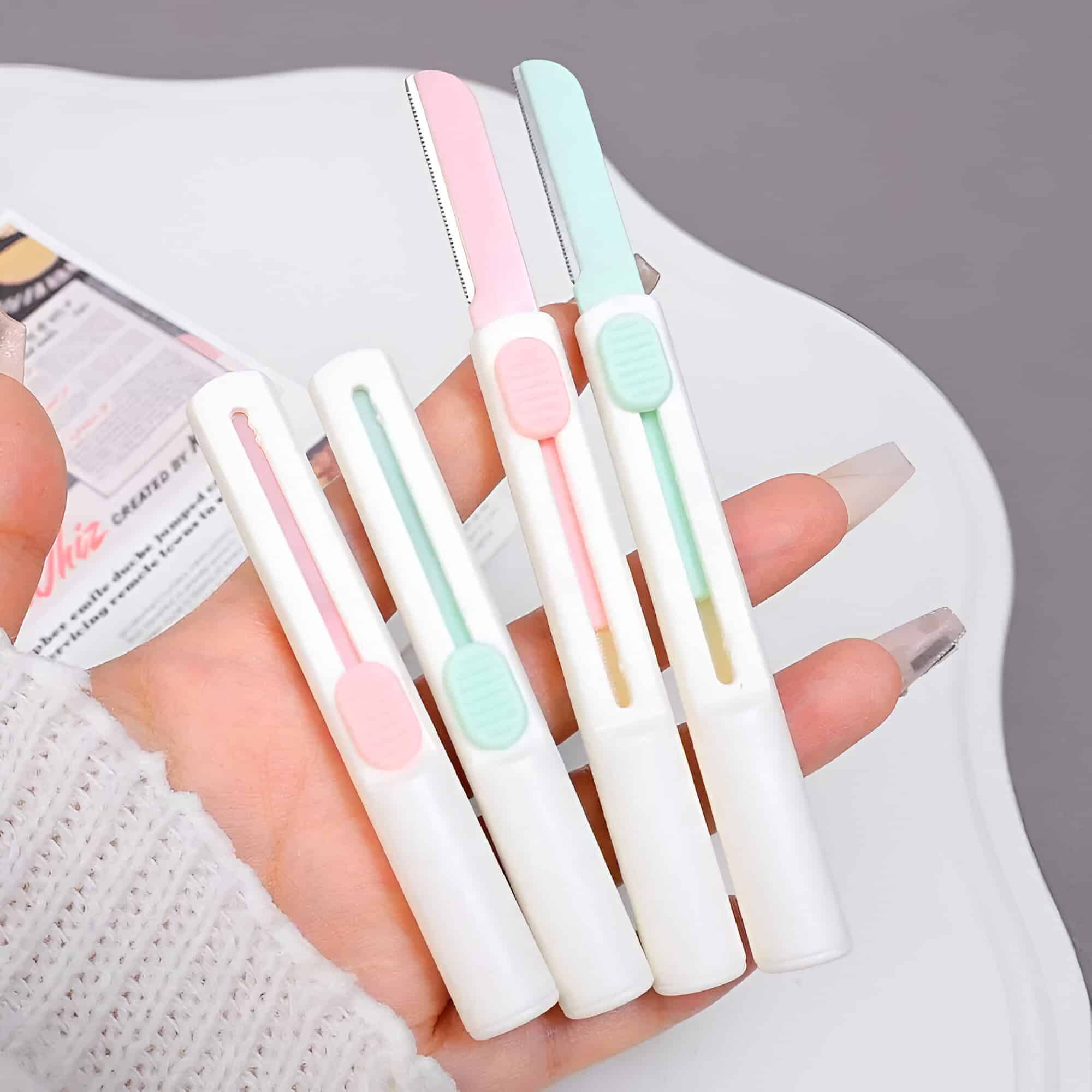 Colorful retractable utility knives in pastel pink, blue, and white, showcased on a person's hand for versatile crafting, office, or household use.