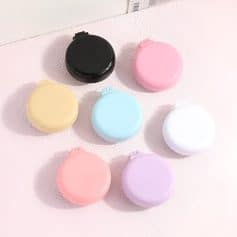 Pink, blue, yellow, black, white, and lavender contact lens cases arranged on a light surface.