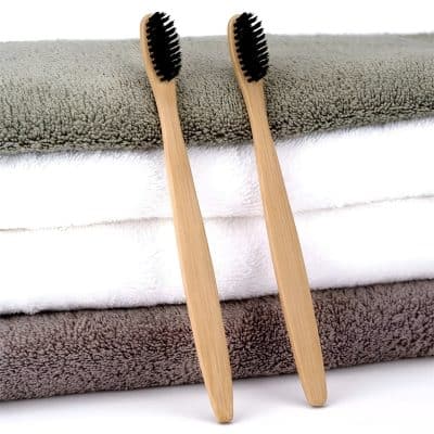 Smooth bamboo toothbrushes with black bristles, eco-friendly and sustainable dental care tools, placed on plush folded towels for a natural and health-conscious appearance.