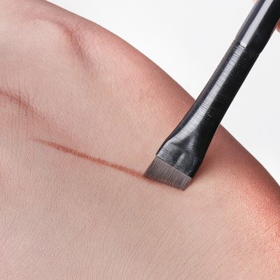 Close-up of a black cosmetic brush applying pigment to the skin, illustrating precision skincare or aesthetic procedures at Monalisa Medical Store.