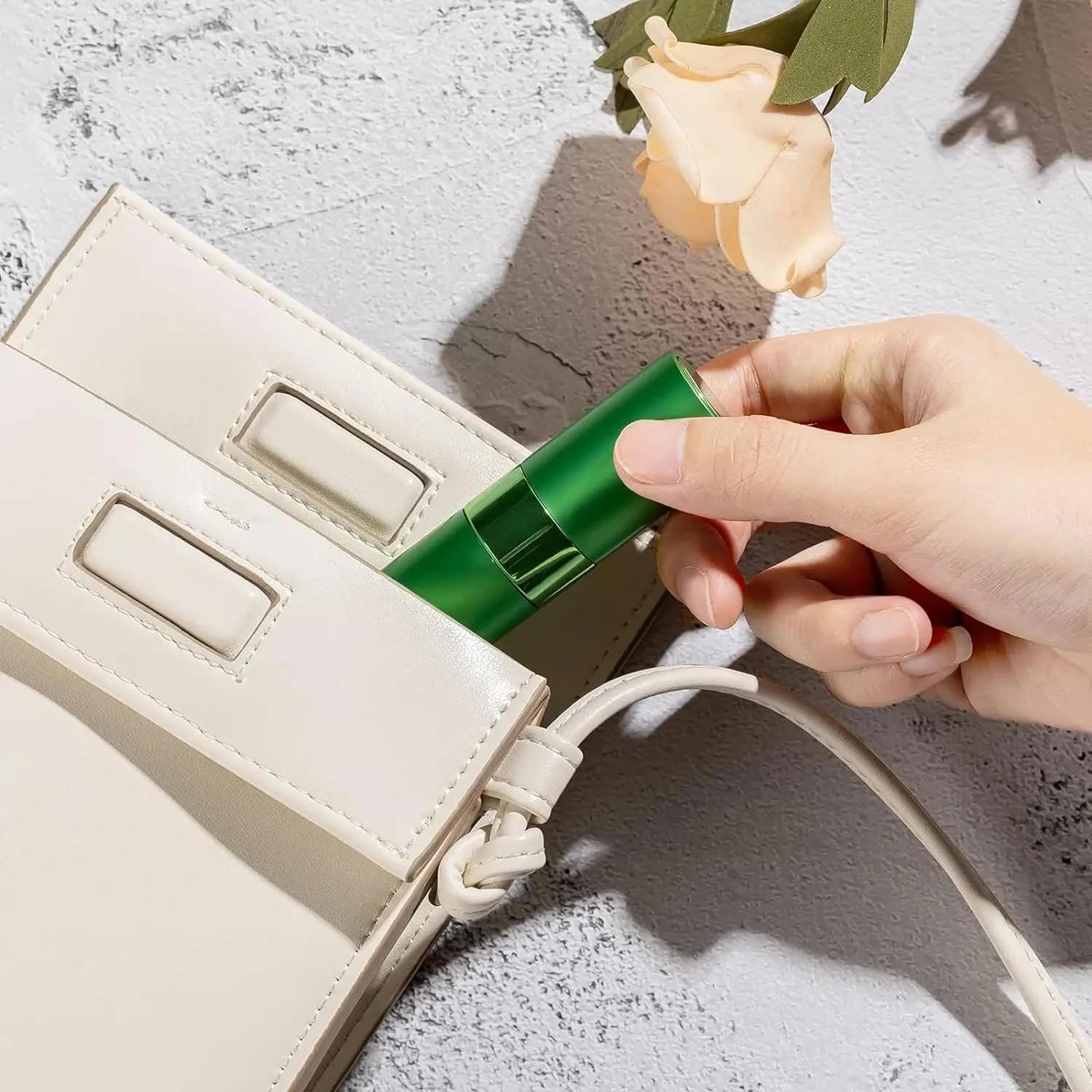 Silicone facial device being placed into a white handbag on a textured surface with a beige flower; skincare essentials, beauty accessories, and luxury beauty products from Monalisa Store.